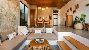 A modern living room with a stone wall, a wooden ceiling, a sofa, a dining table, and a kitchen area. - Charming 1-bedroom villa with swimming pool (Tibubeneng)