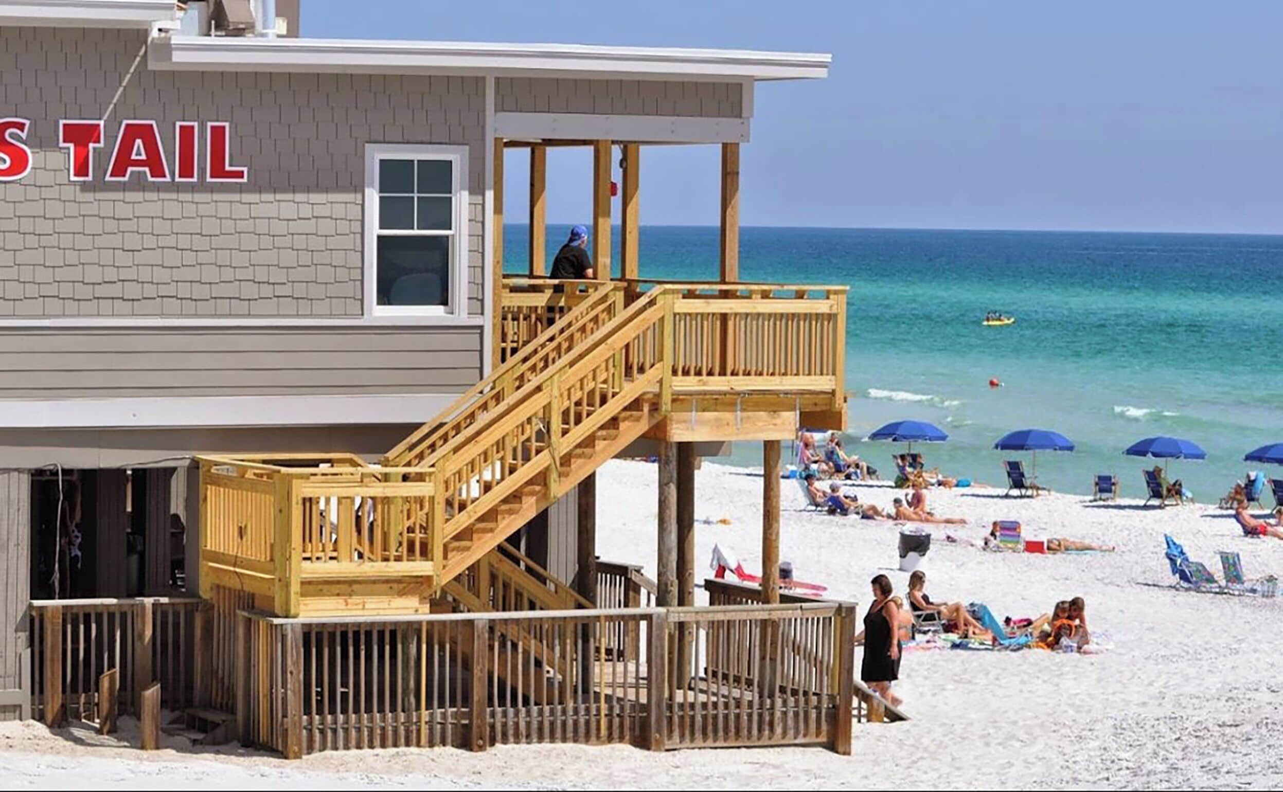 Ein Gebäude am Strand mit einem Rettungsturm, einer Holzterrasse und Strandliegen.