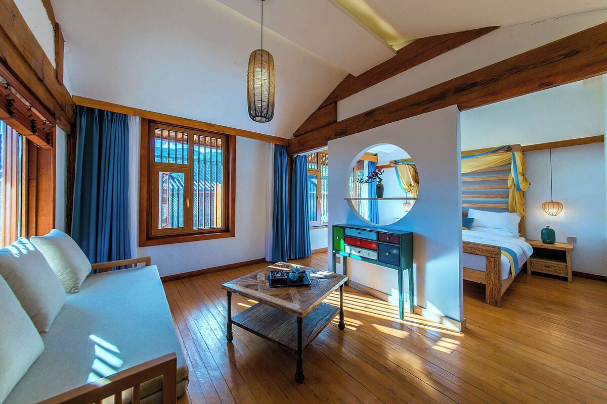 Ein Zimmer mit Holzboden, einer Couch, einem Tisch mit einer Vase, einem Bett und einem Nachttisch mit einer Lampe.