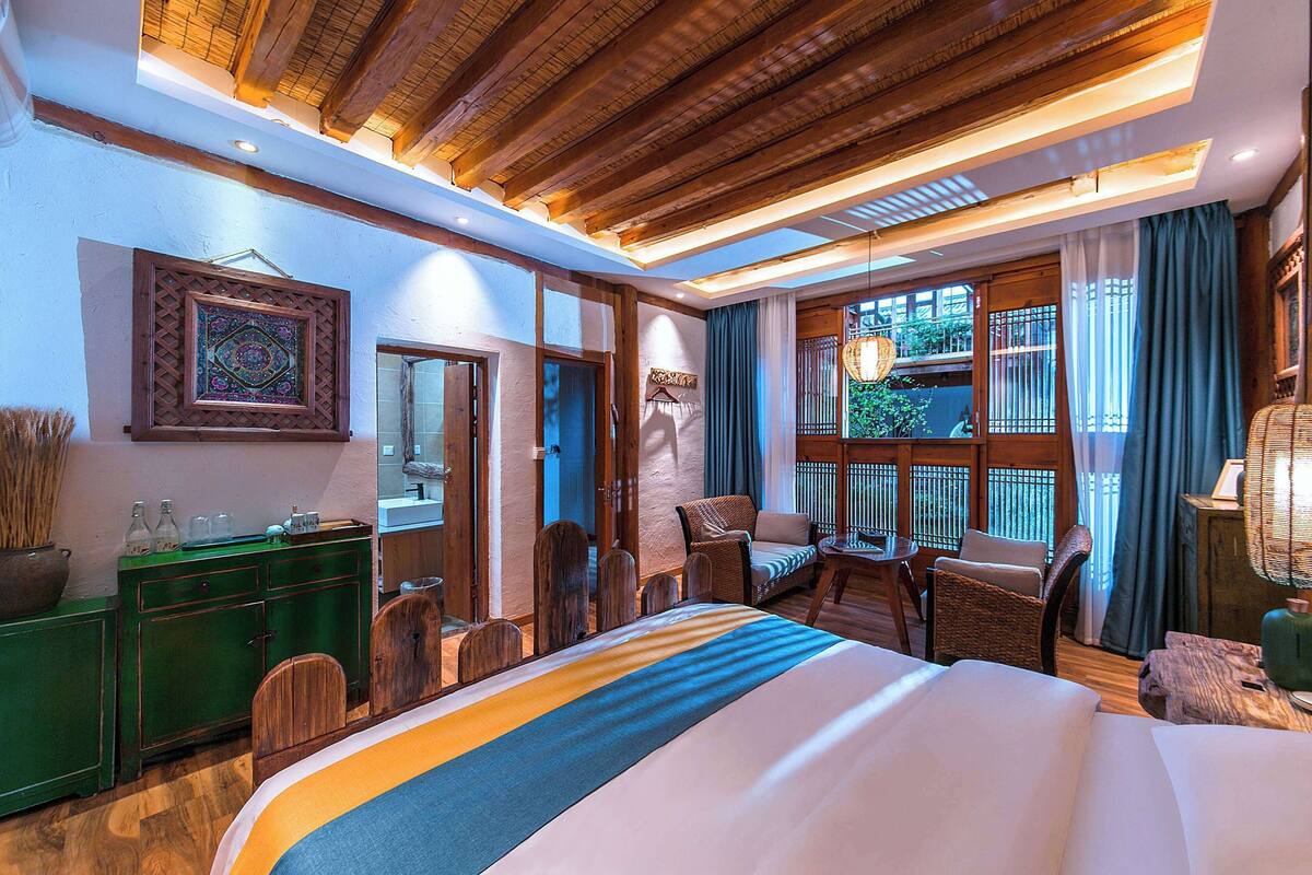 Ein Hotelzimmer mit einem großen Bett, Holzbalkendecke, einem grünen Schrank, Korbmöbeln und großen Fenstern.