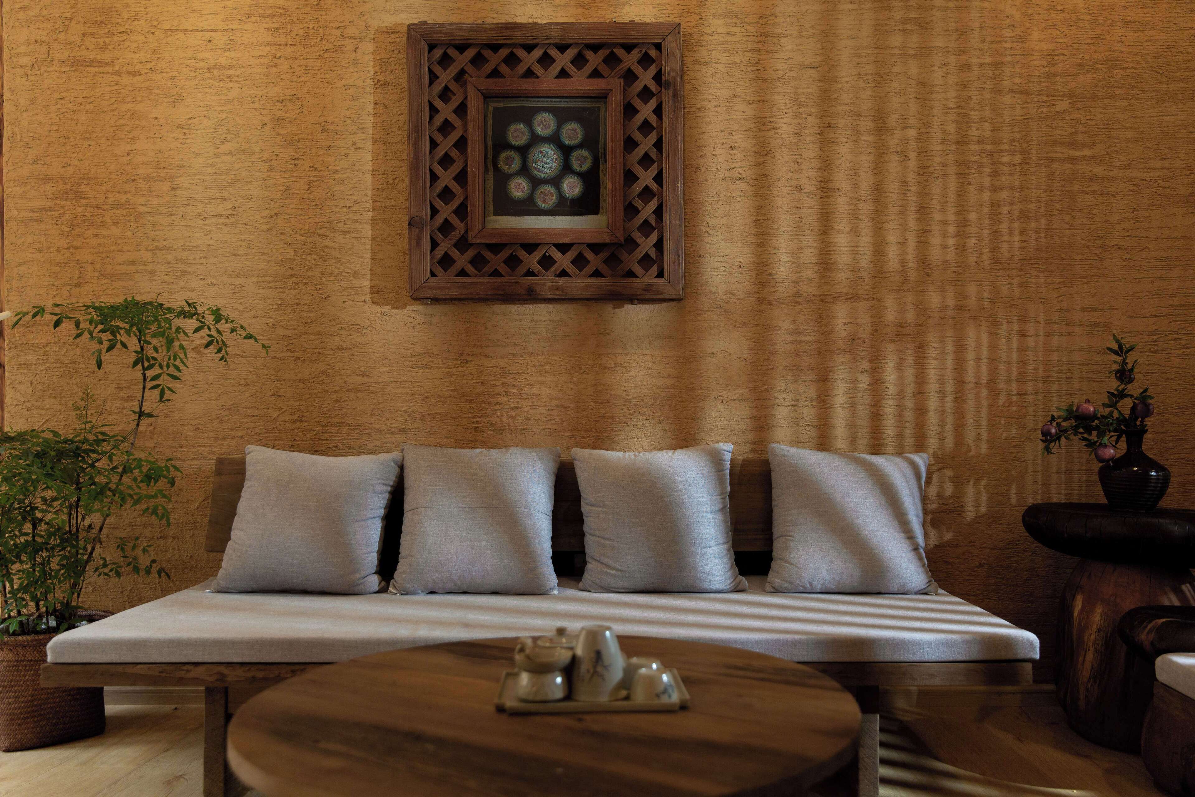 A room with a wooden wall, a sofa with cushions, a small table with a teapot, and a potted plant.