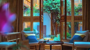 A room with large windows, wooden furniture, and a view of greenery outside.