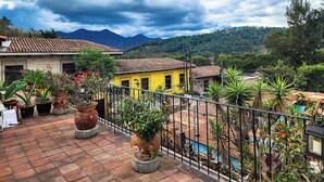 A courtyard with potted plants, a yellow building, and a view of mountains under a cloudy sky.