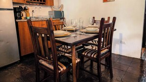 A dining area with wooden chairs and a table set for four. There is a kitchen area with wooden cabinets and a refrigerator.