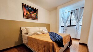 A neatly made bed with a brown bedspread and a black throw blanket, white pillows, and a framed painting above the bed.