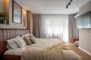 A modern bedroom with a large bed, a potted plant, and a mounted TV.