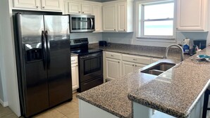 Una cocina moderna con armarios blancos, electrodomésticos de acero inoxidable, encimeras de granito y un ventanal que proporciona luz natural.