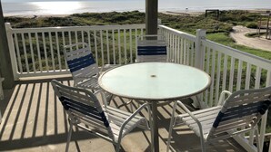 Un espacio al aire libre cubierto con una mesa, sillas, una valla blanca y vistas a la playa y al océano.