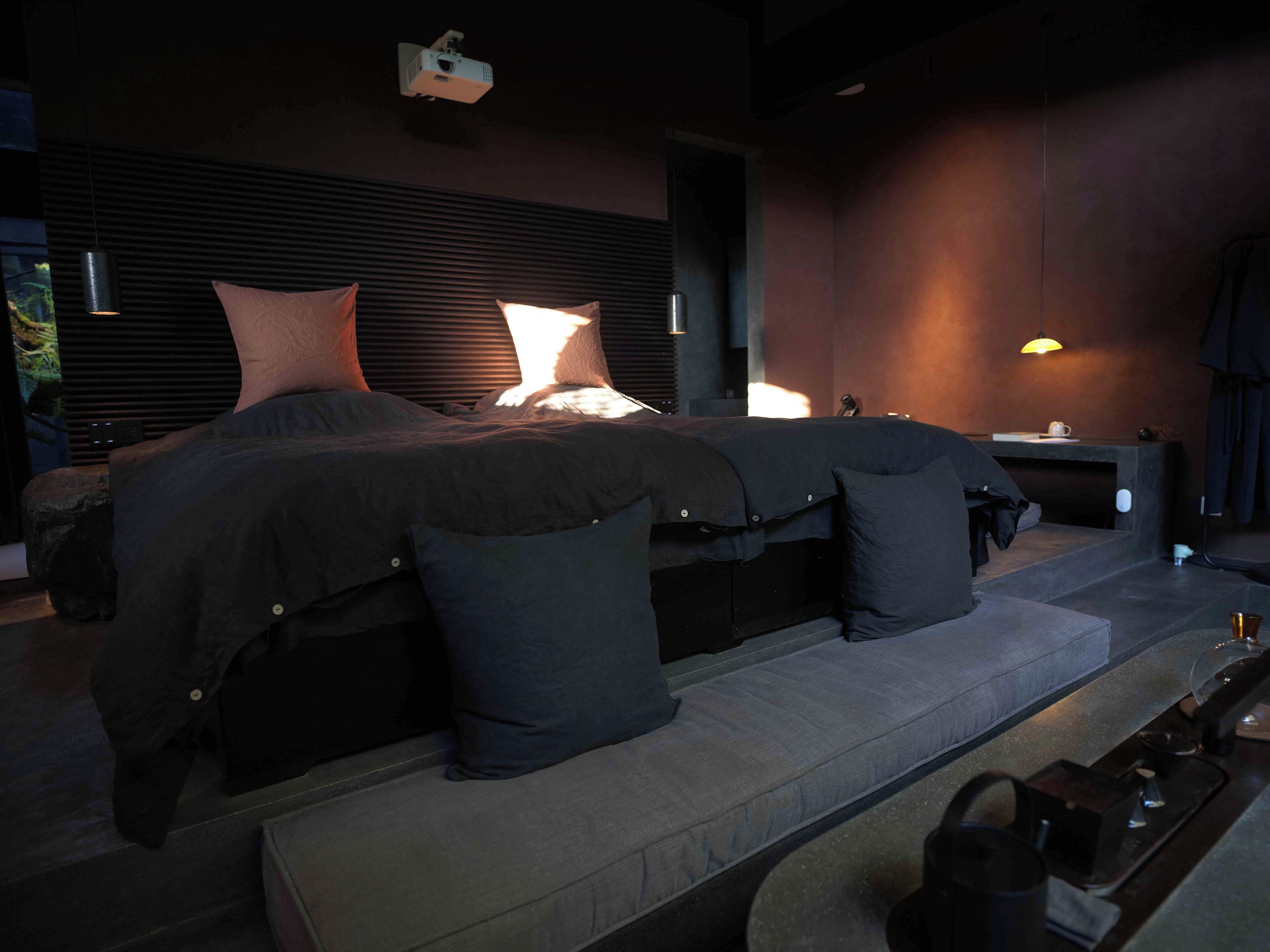 A modern bedroom with a large bed, bedside tables, and a projector mounted on the ceiling.