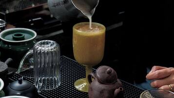 A kitchen with a coffee maker, a teapot, and a glass of a yellowish beverage being poured.
