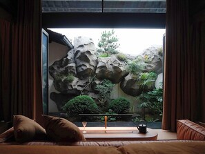 A room with a bed, a bedside table with a glass, and a view of a rock garden with plants. - Stayinmind (Xuancheng)