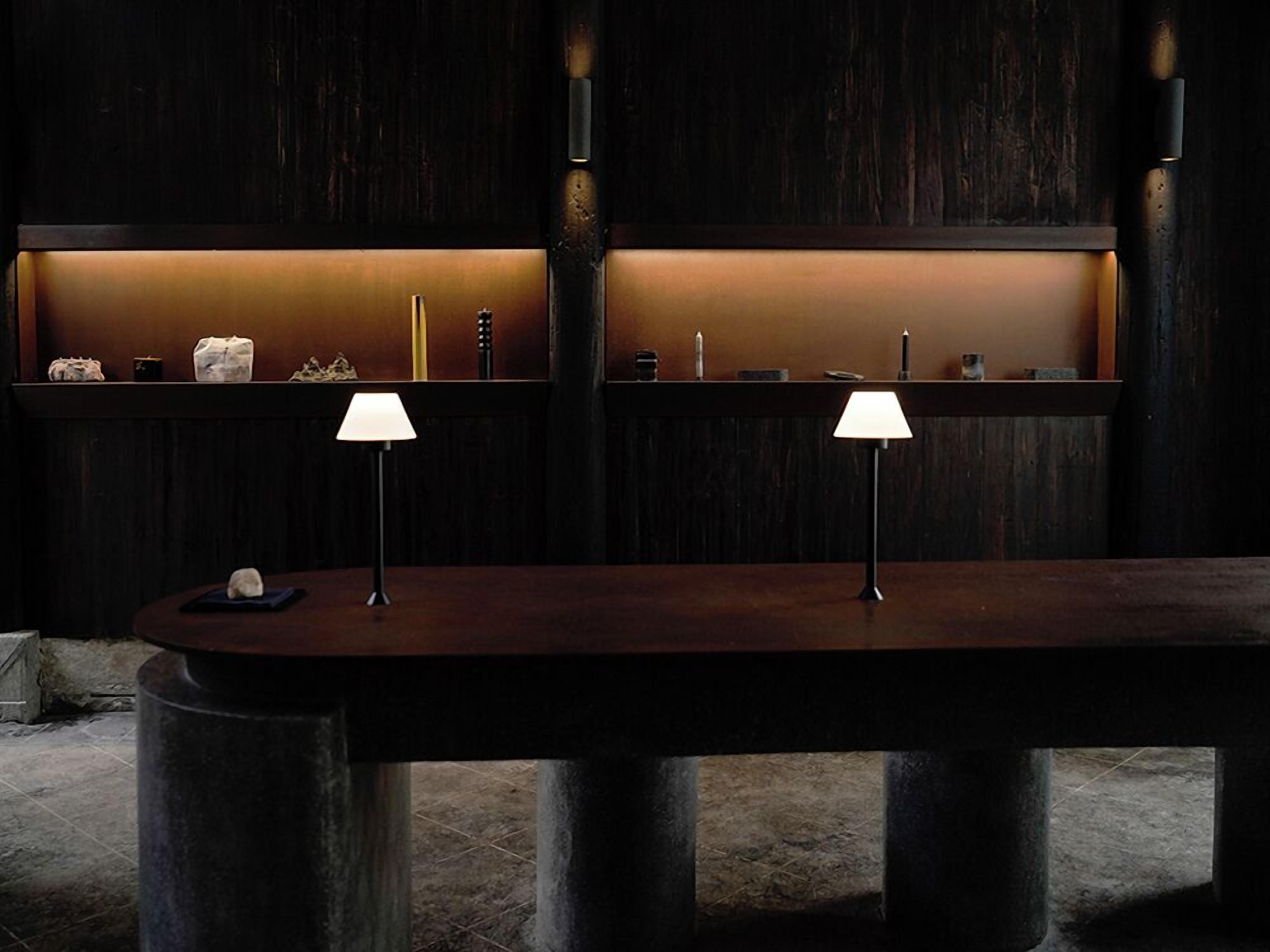A reception desk with two lamps, a wooden counter, and a dark wooden wall with a shelf above.