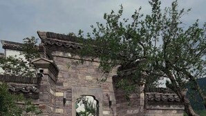 A stone archway with intricate carvings, surrounded by greenery and a stone pathway. - Stayinmind (Xuancheng)