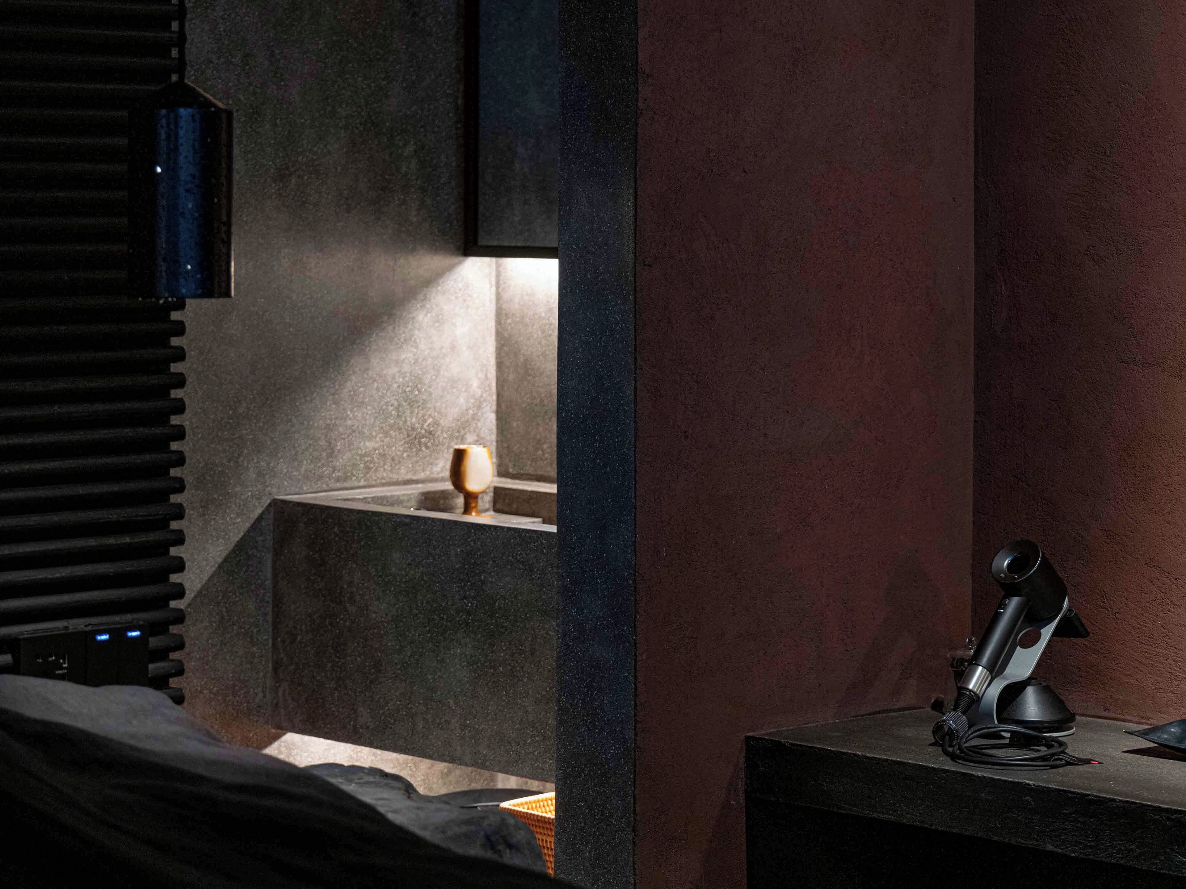 A dimly lit room with a bed, a small table with a microphone, and a cup on a shelf.
