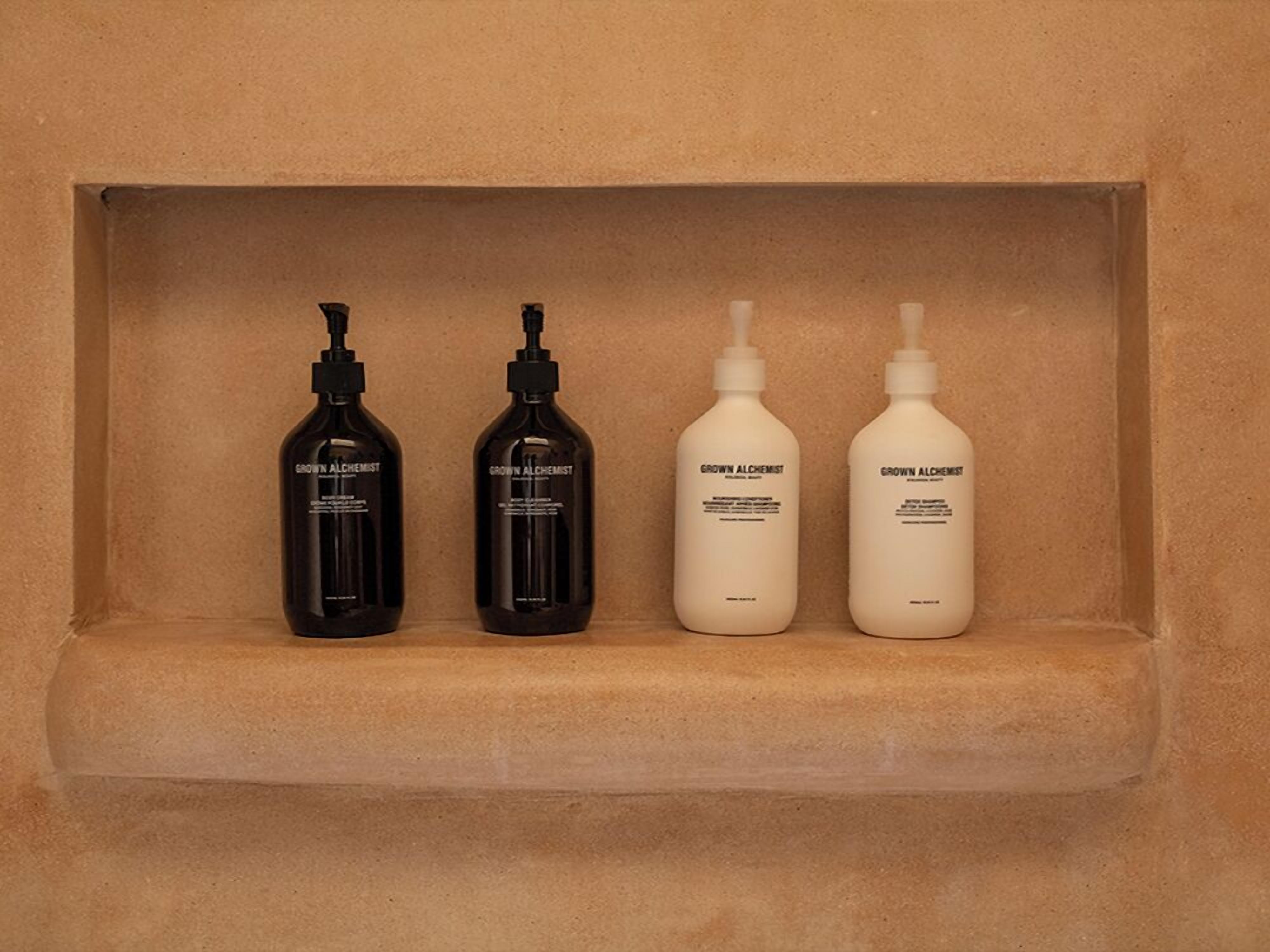 Trois flacons de produits de soins pour la peau de la marque « Grown Alchemist » sont posés sur une étagère beige.