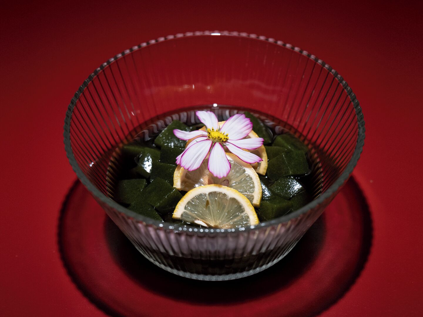 A clear glass bowl containing green items, possibly vegetables, with a flower and lemon slices on top.