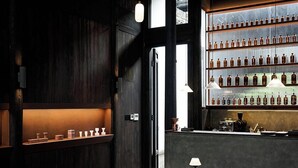 A bar area with wooden shelves displaying bottles, a counter with bar equipment, and two stools with lamps. - Stayinmind (Xuancheng)