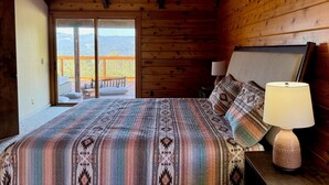 Un dormitorio con una cama grande, una mesita de noche, una lámpara y vistas a un balcón con mobiliario exterior.