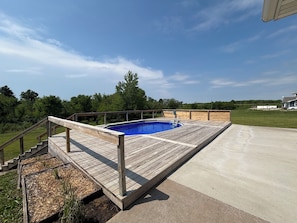 A wooden deck surrounding a swimming pool with a concrete patio adjacent to it.