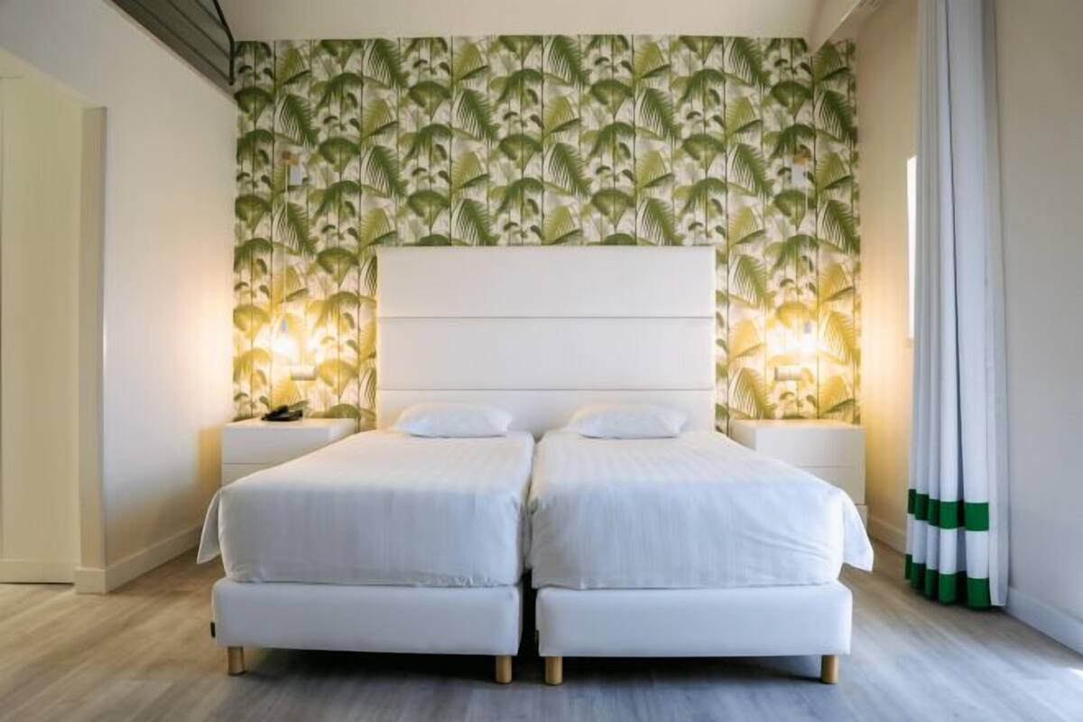 Una cama doble con cabecera blanca, dos mesitas de noche y papel tapiz estampado.