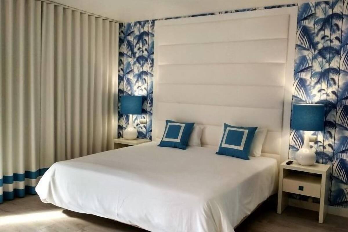 Una habitación de hotel con una cama grande, dos mesitas de noche y un cabecero.