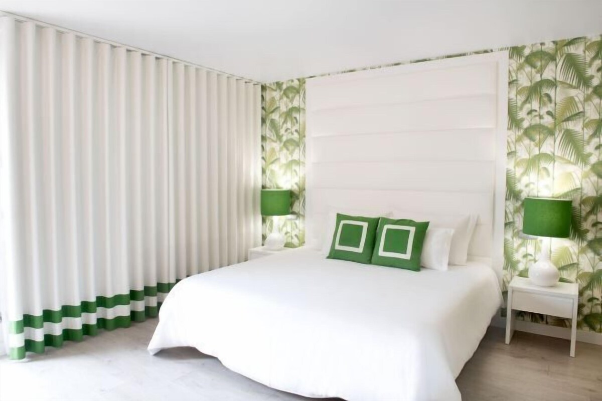 Une chambre à coucher avec un grand lit, deux tables de chevet et une fenêtre avec des rideaux.