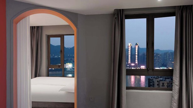 Ein Hotelzimmer mit Bett, einem Fenster mit Vorhängen und Blick auf Stadtgebäude.
