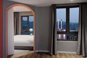 Habitación de hotel con cama, ventana con cortinas y vistas a edificios de la ciudad.