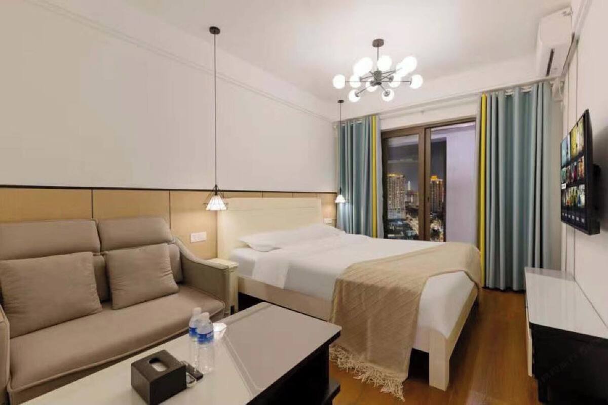 A hotel room with a bed, a sofa, a bedside table, a TV, and a window with curtains.
