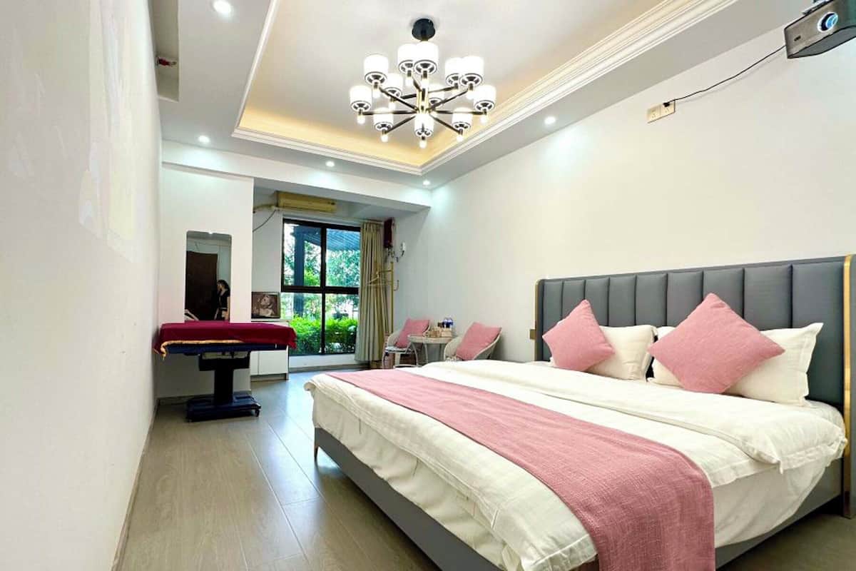 A modern bedroom with a large bed, a massage table, and a view of greenery outside.