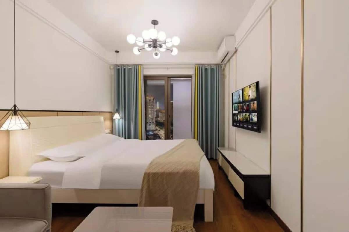A hotel room with a bed, bedside table, lamp, and a TV mounted on the wall.
