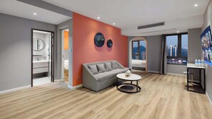 Ein modernes Wohnzimmer mit einem karierten Sofa, einem runden Couchtisch und Blick auf die Stadt durch große Fenster.