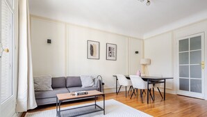 A living room with a sofa, coffee table, and dining table with chairs. - Blueground | Porte Dauphine, balcony, nr Bois de Boulogne (Paris)