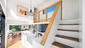 A modern kitchen with a wooden staircase, a dining area, and a view of greenery outside. - Mountain View Retreat Near Wanaka - Cosy Tiny Home Cottage (Hāwea Flat)