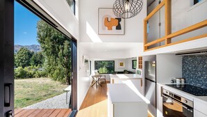 A modern kitchen with a large island, wooden flooring, and a view of the outdoors. - Mountain View Retreat Near Wanaka - Cosy Tiny Home Cottage (Hāwea Flat)
