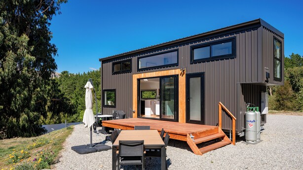 A modern house with a deck, outdoor seating, and a gas cylinder. - Mountain View Retreat Near Wanaka - Cosy Tiny Home Cottage (Hāwea Flat)
