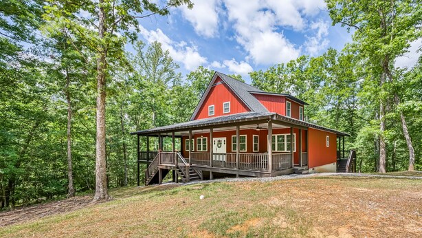 Une cabane rouge avec un porche, entourée d’arbres.