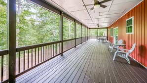Une véranda couverte avec un plancher en bois, un ventilateur de plafond et une vue sur une zone boisée.