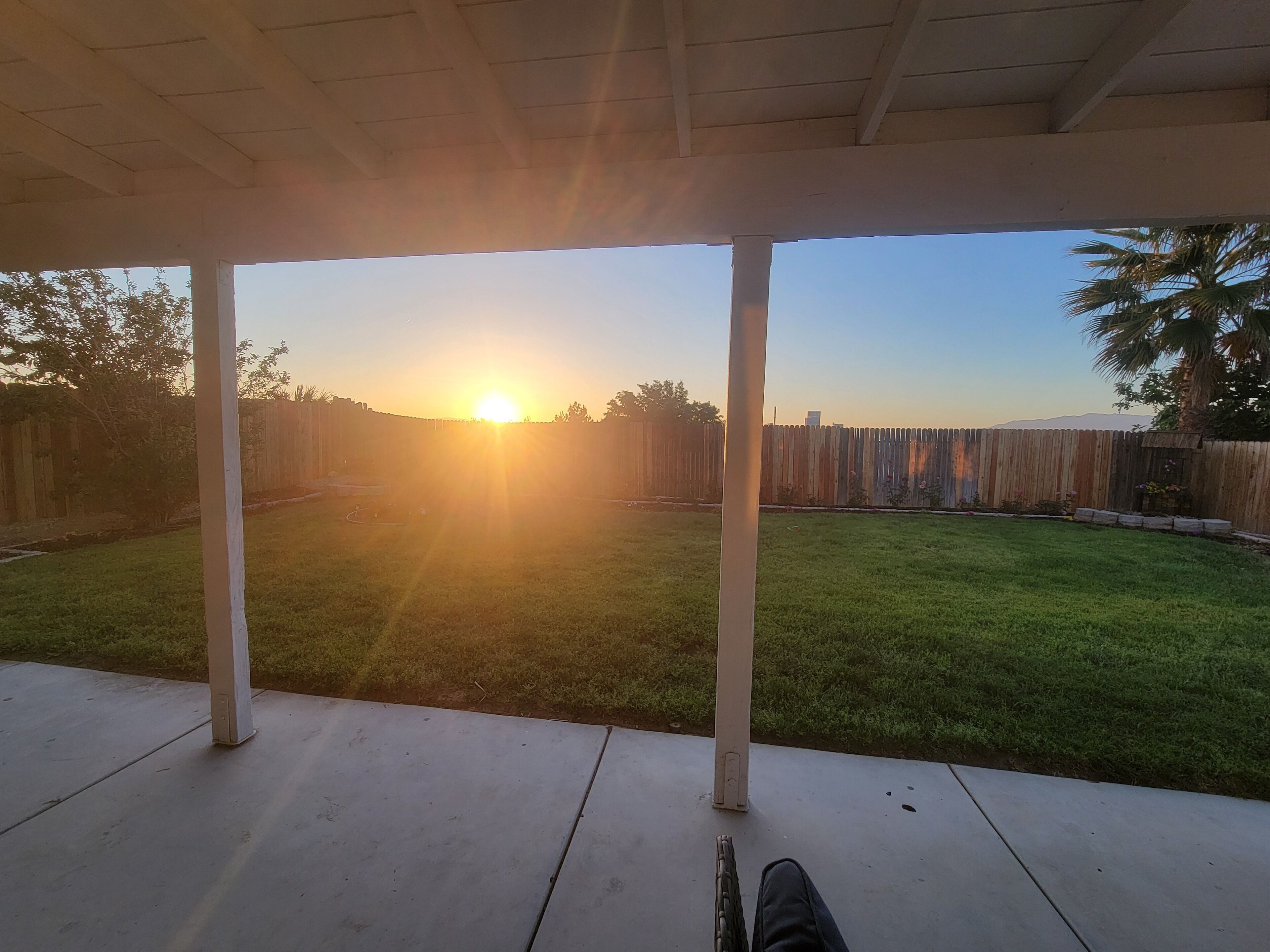 A covered patio area with a view of a grassy backyard and a wooden fence.