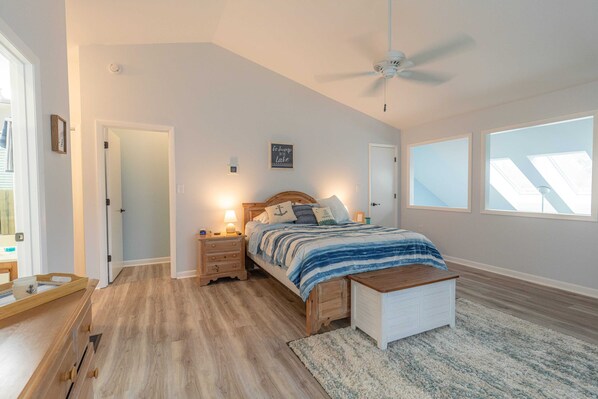 A bedroom with a bed, bedside tables, a nightstand, a wooden bench, a ceiling fan, and a skylight.