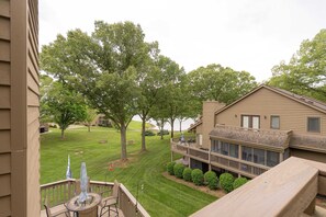 A residential area with a two-story house featuring a balcony with outdoor seating and a view of a well-maintained lawn and trees.