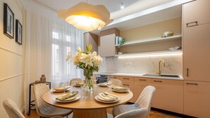 A modern dining area with a round table set for four, a vase of flowers, and a kitchen in the background.