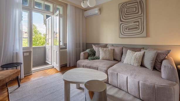 A living room with a beige sofa, a round coffee table, and a view through a large window.