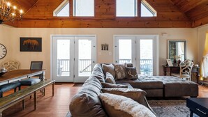 Ein geräumiges Wohnzimmer mit Holzbalkendecke, einem großen Ecksofa, einem Esstisch mit Bänken und einer Chandelüster.