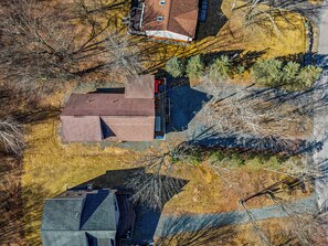 An aerial view of a residential area with multiple houses, a paved driveway, and surrounding trees.