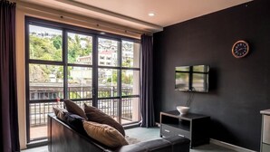 Ein modernes Wohnzimmer mit großem Fenster, einer schwarzen Couch, einem Fernseher und einem kleinen Tisch.