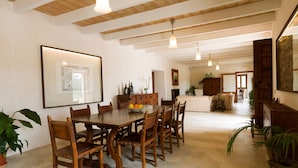 Un grand espace dédié à la salle à manger, avec une table et des chaises en bois, un tableau encadré au mur et une cuisine en arrière-plan.