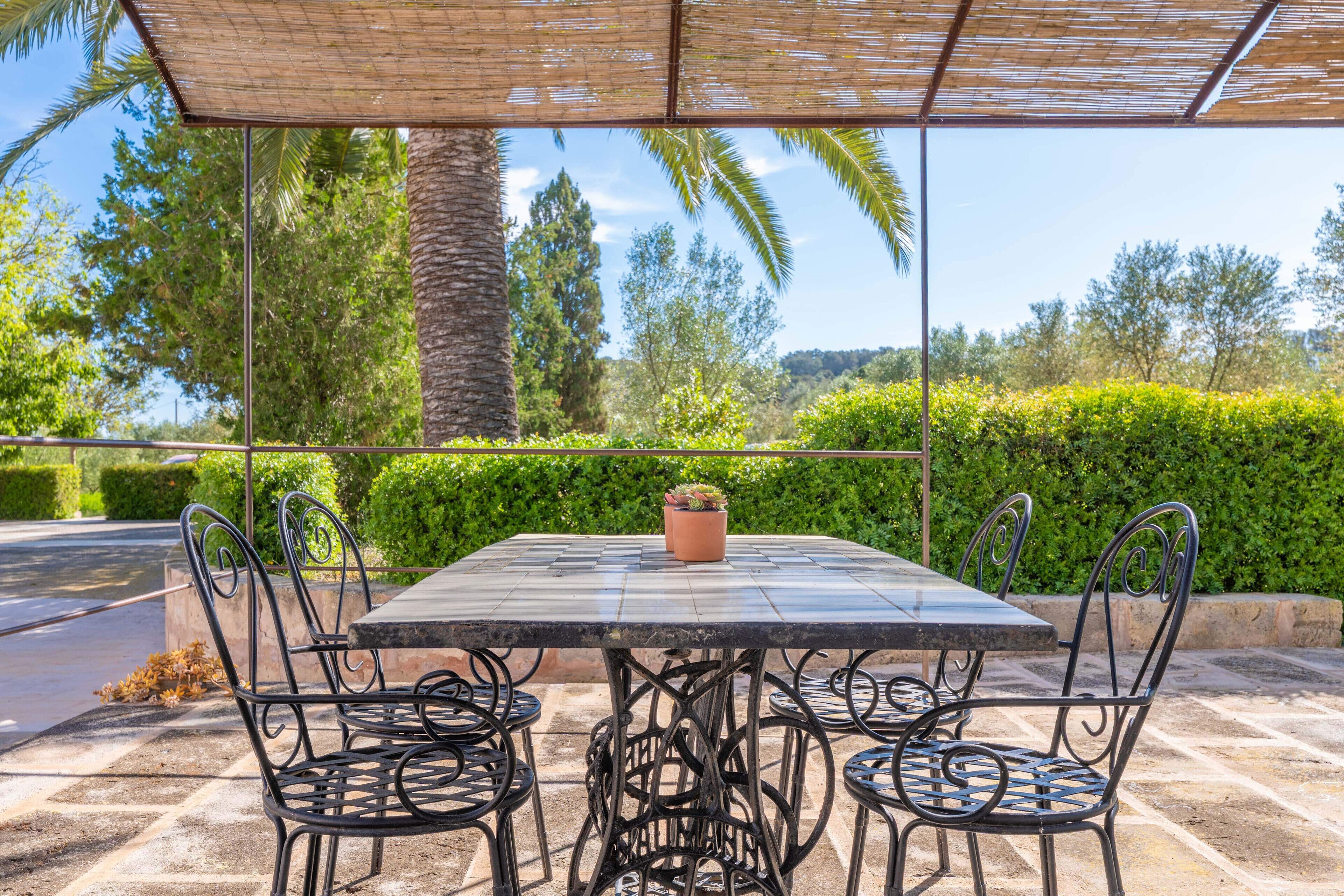 An outdoor patio with a table and chairs, surrounded by greenery and a clear sky.