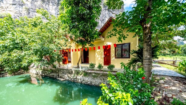 A building with a stone wall, a small pool, and greenery. - Tràng An Sunny River Homestay (Ninh Binh)