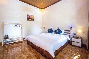 A hotel room with a wooden bed, a bedside table with a lamp, a wall-mounted shelf with hangers, and a painting on the wall. - Tràng An Sunny River Homestay (Hoa Lu)